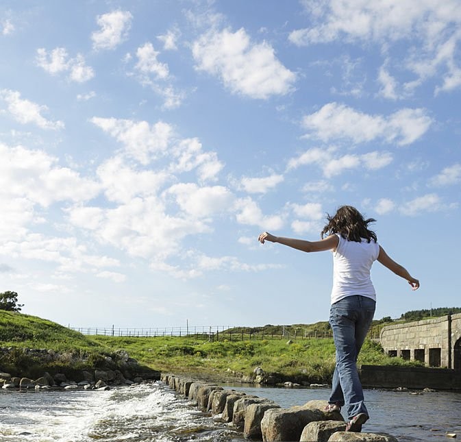 Young girl runs across stepping stones  to cross a stream